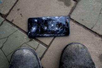 Cracked phone laying on bricks on the ground, next to a pair of feet.
